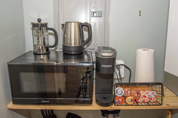 Een kitchenette met een magnetron, koffiezetapparaat en een koffiemolen op een houten plank.