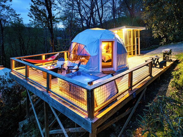 A wooden deck with a tented sleeping area, a small table, and a grill.