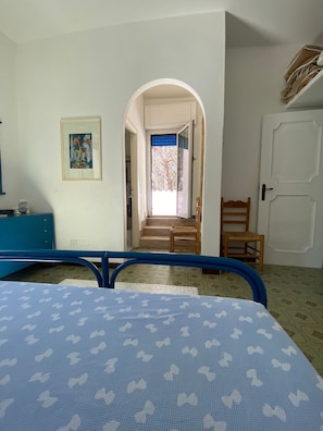 A bedroom with a bed, a desk, a chair, a door, and a staircase leading to a balcony. - Splendid Detached Villa, Near the sea (Siniscola)