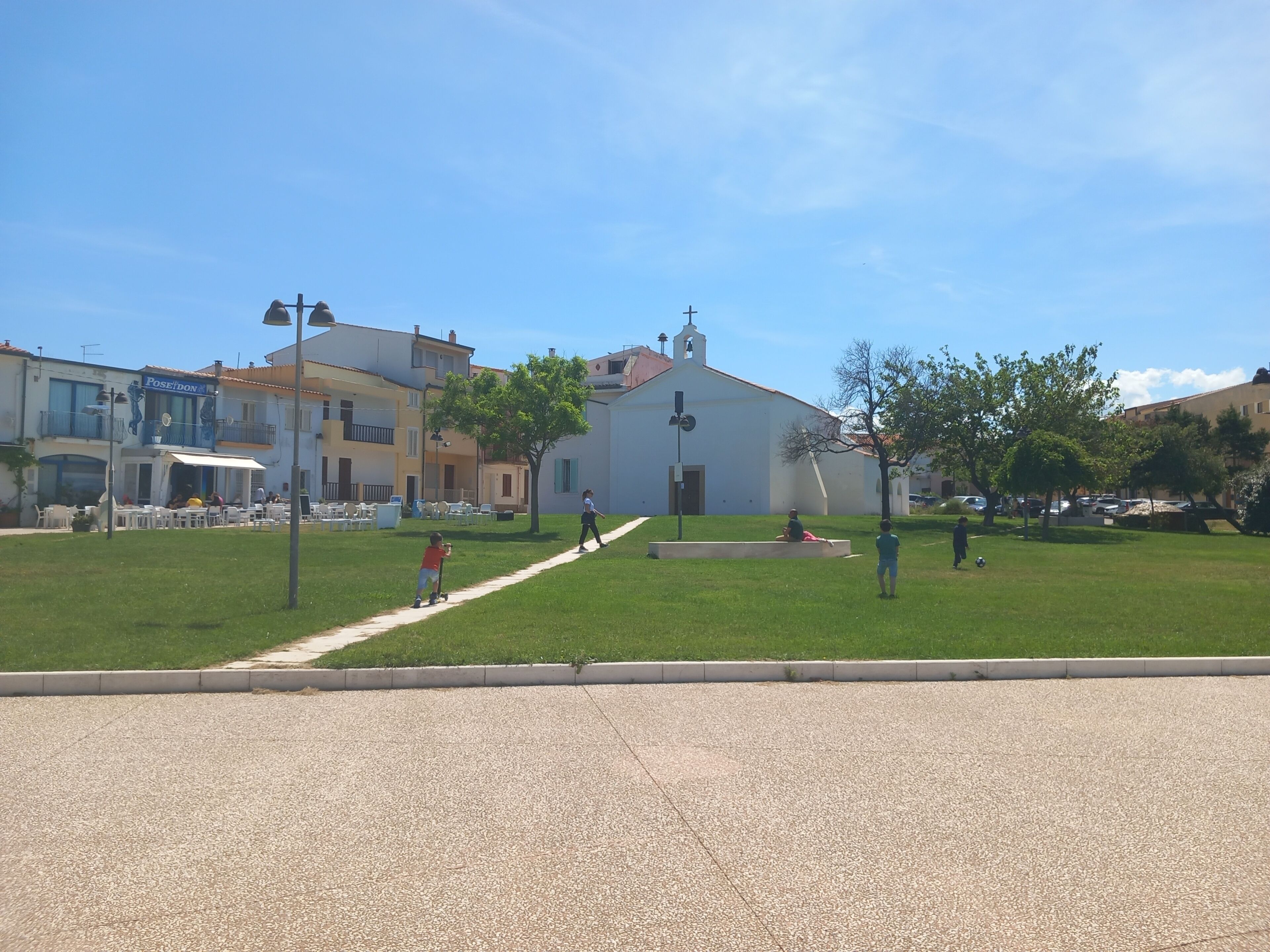 A paved square with a grassy area, a church, and buildings with balconies.