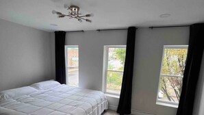 Un dormitorio con una cama grande, dos ventanas y un ventilador de techo.