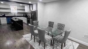 Una cocina moderna con armarios blancos, un refrigerador de acero inoxidable y un comedor con mesa de vidrio y sillas tapizadas en gris.