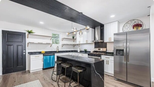 Una cocina moderna con una isla central, taburetes de bar, un refrigerador de acero inoxidable y un techo negro.