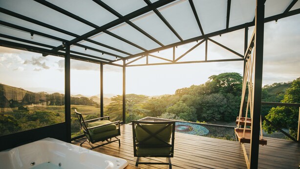 Una terraza de madera con un jacuzzi y dos sillas, con vistas a un paisaje exuberante.