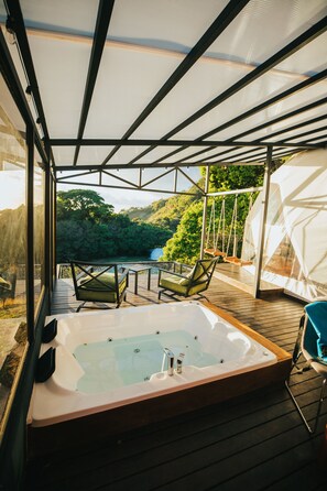 Un bain à remous avec une terrasse en bois et des chaises, donnant sur une zone boisée.