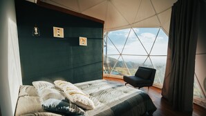 Un dormitorio con una cama grande, una silla y vistas al exterior a través de una ventana de formas geométricas.