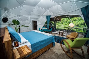 Une pièce aménagée comme une tente, avec un lit, une table, des chaises et une vue sur la verdure environnante.