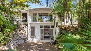 A two-story house with a balcony, surrounded by lush greenery and a stone wall. - Belle Escapes Sandpipers Beach House (Palm Cove)
