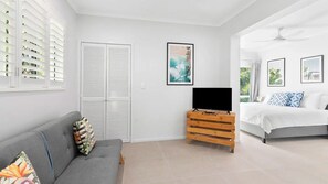 A modern bedroom with a grey sofa, a wooden dresser, a bed with white bedding, and a TV on a wooden stand.