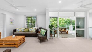 A modern living room with a sofa, coffee table, and a dining area with a table and chairs. - Belle Escapes Sandpipers Beach House (Palm Cove)