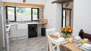 Une cuisine compacte équipée d’un lave-linge, un coin repas avec une table mise pour le petit-déjeuner, et une vue par la fenêtre.