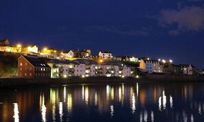 A waterfront town at night with illuminated buildings reflecting on the water.