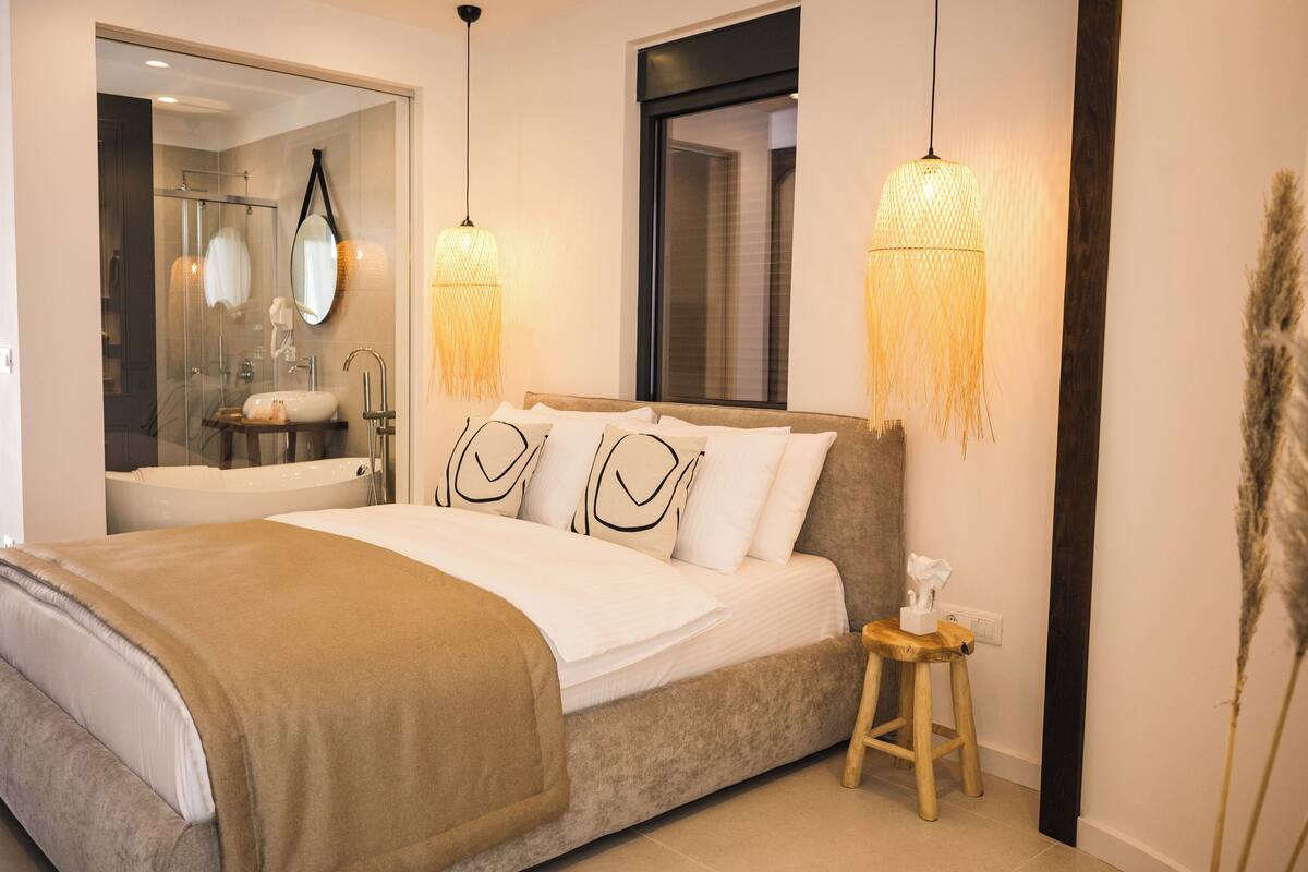 A bedroom with a bed, bedside table, and a bathroom visible through a glass door.
