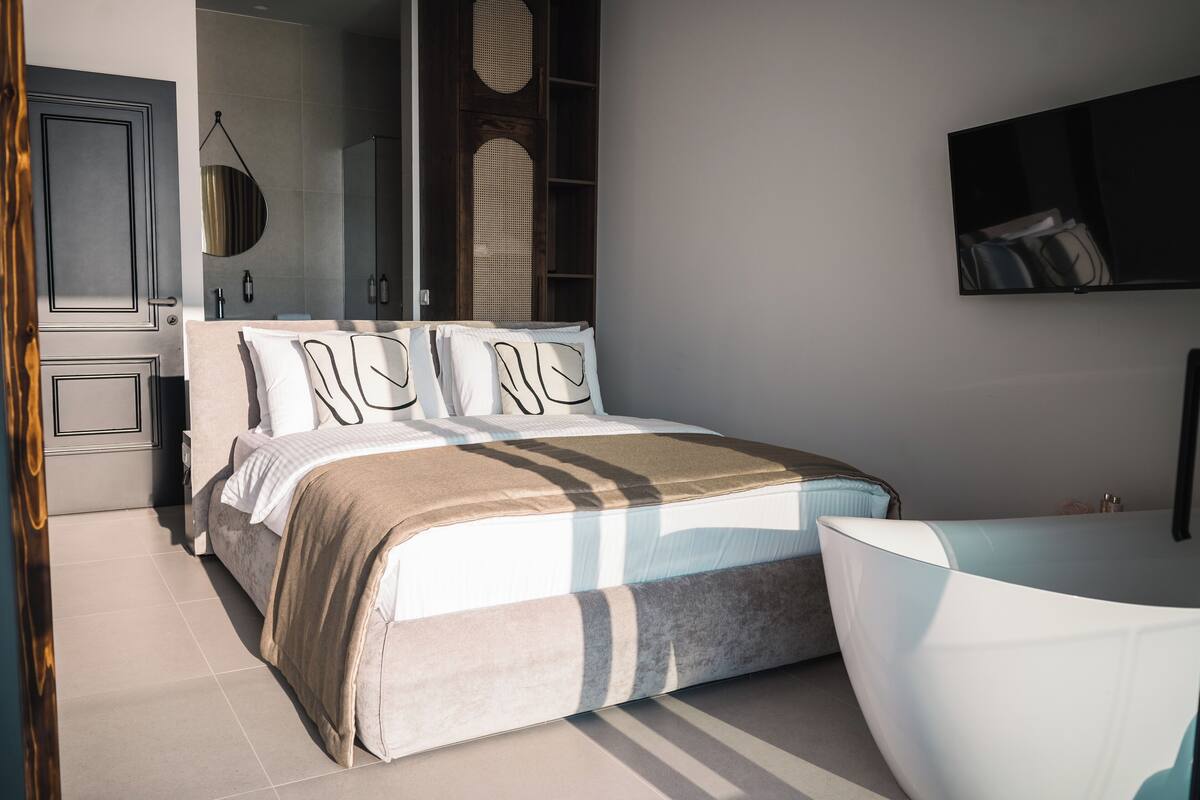 A modern bedroom with a large bed, a built-in wardrobe, a mirror, and a TV mounted on the wall.