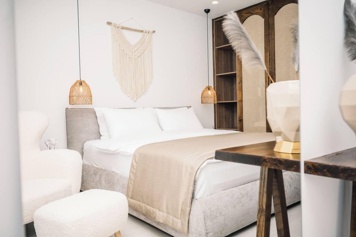 A modern bedroom with a bed, two bedside lamps, a macrame wall hanging, and a wooden wardrobe.