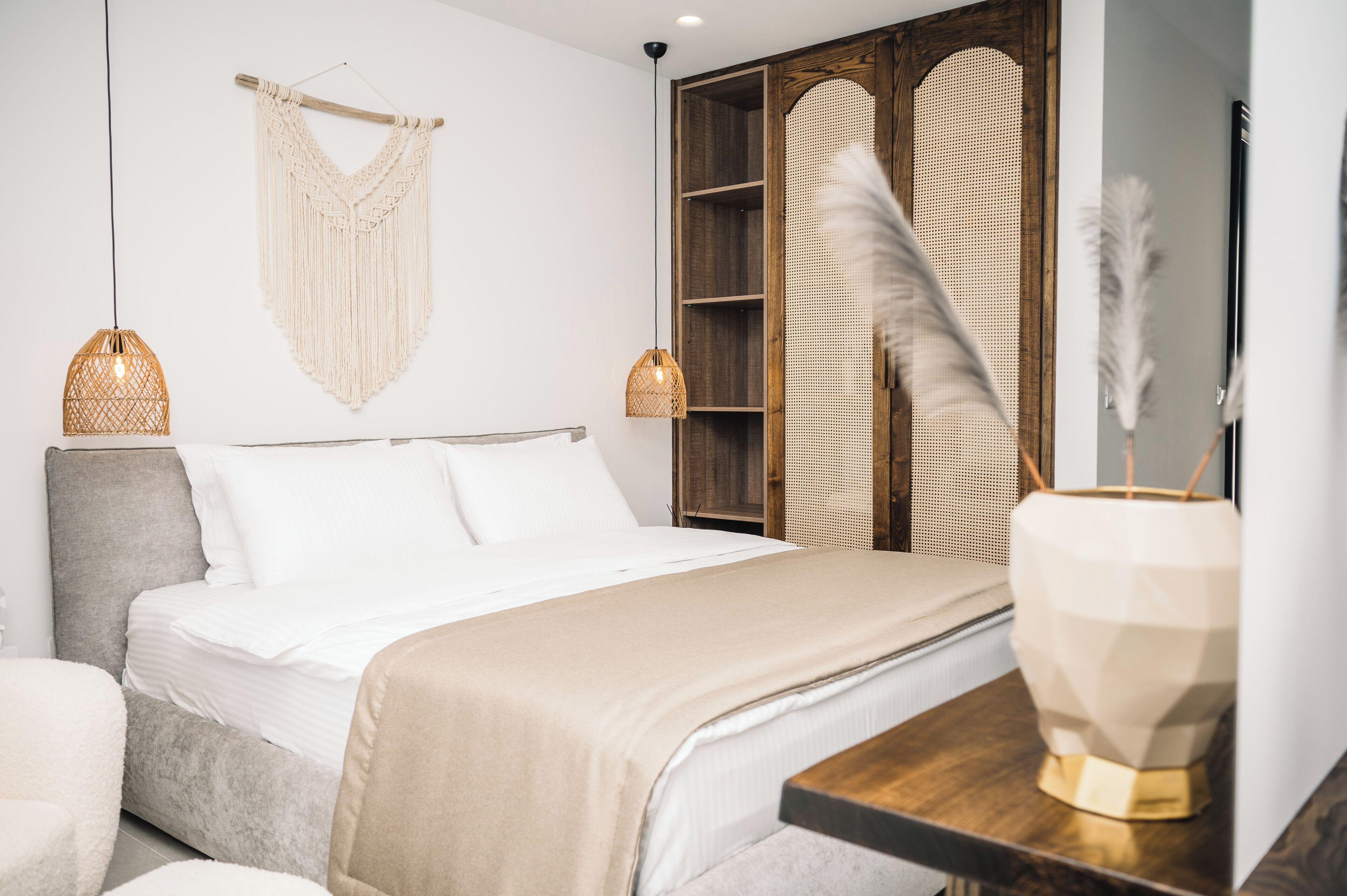 A modern bedroom with a bed, bedside lamps, a macrame wall hanging, and a woven basket.