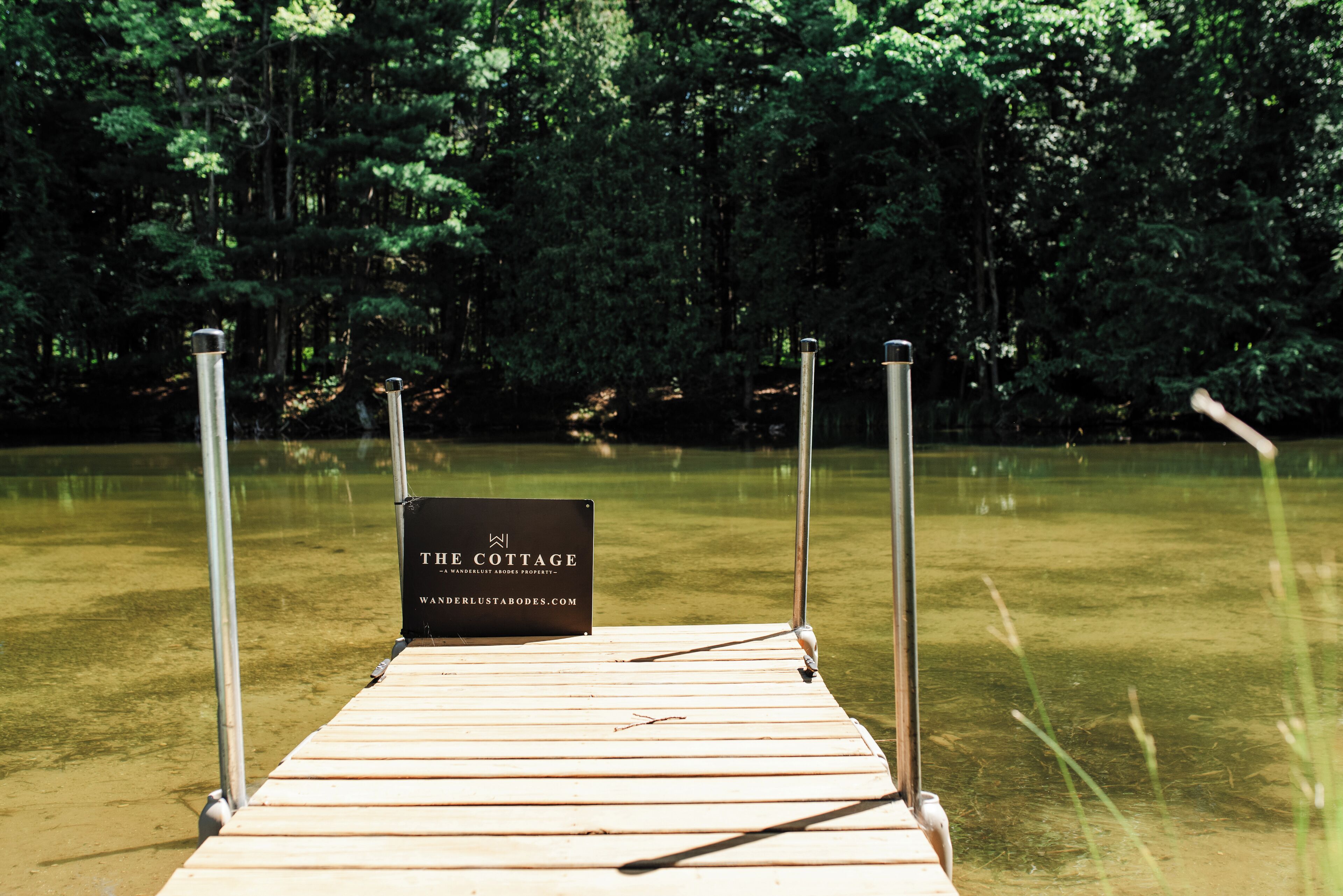 A wooden dock leading into a lake with a sign that reads "The Cottage."