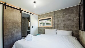 A modern hotel room with a large bed, a sliding door, a mirror, and a view of the outside. - The Cottage (Bellaire)
