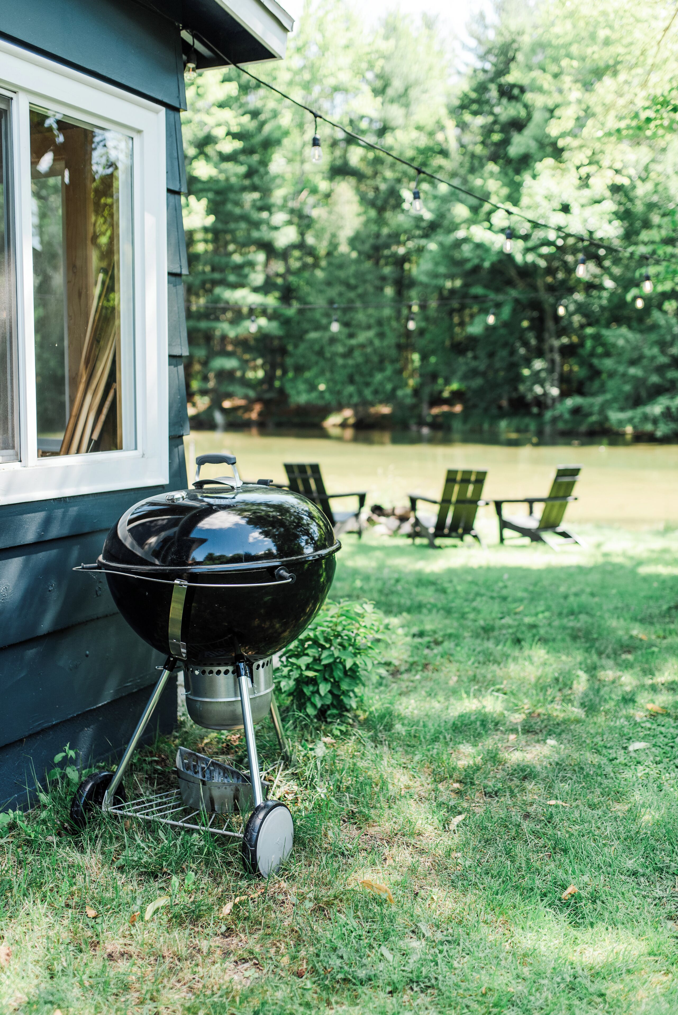 A barbecue grill outside a house with a grassy yard and a pond in the background.