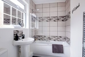 A modern bathroom with a white sink, a mirror, a shower, and a tiled wall with a 'Get Naked' sign.