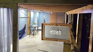 A room with a wooden ceiling, a hammock, a small table with chairs, and a decorative metal panel.