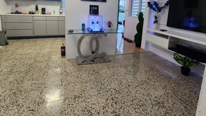 A modern living room with a kitchen area, a mounted TV, and a decorative wall piece.