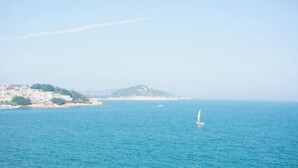 A coastal view with a building complex on a hill and a sailboat in the water. - Dongshan Haizhiyuan Apartment (Dongshan County)