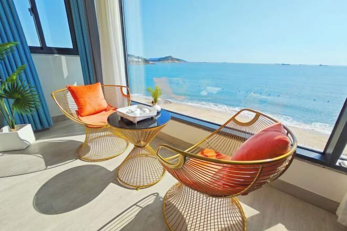 A balcony with a view of the sea, featuring two wicker chairs and a small table with a plant.