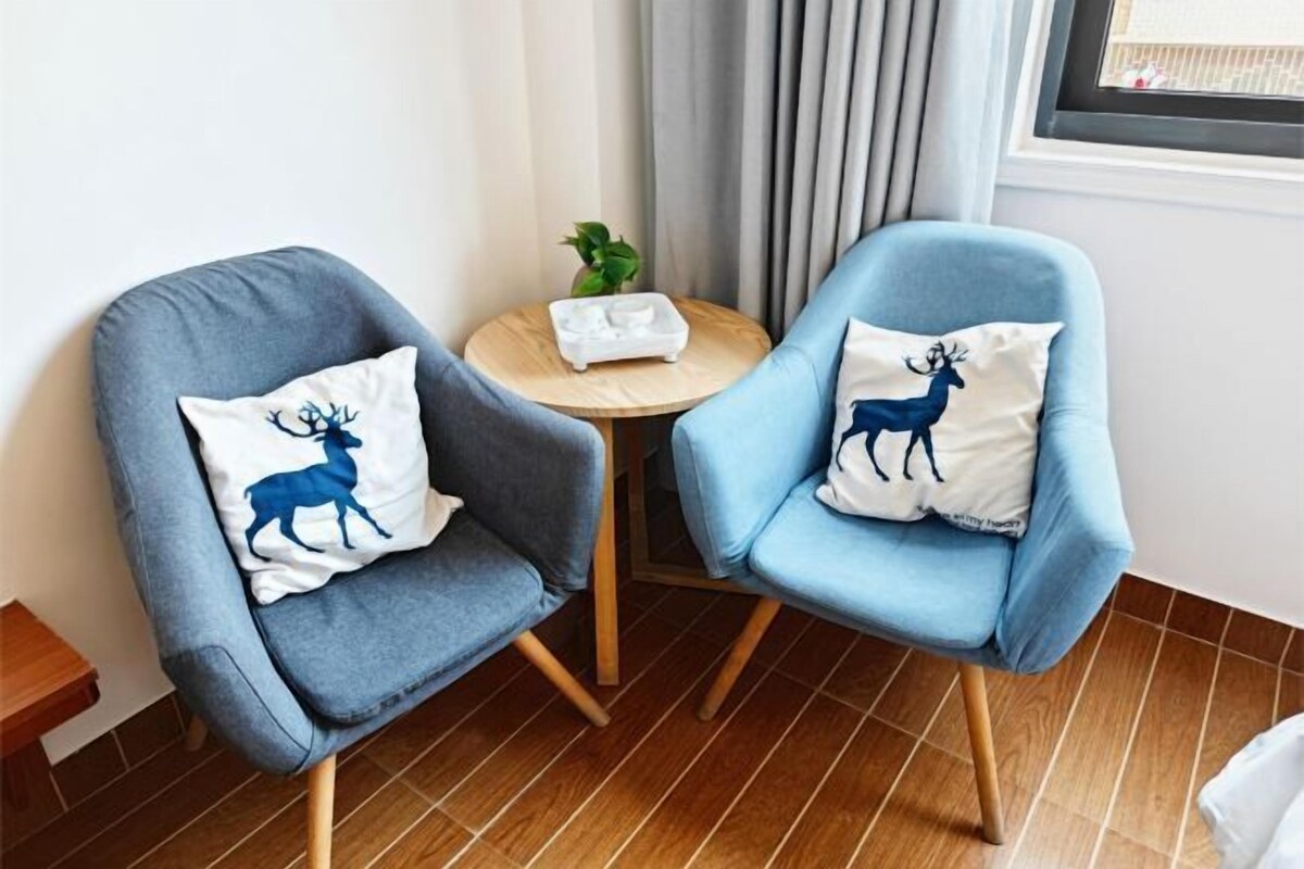 Two armchairs with decorative pillows, a small round table with a plant, and a window with curtains.