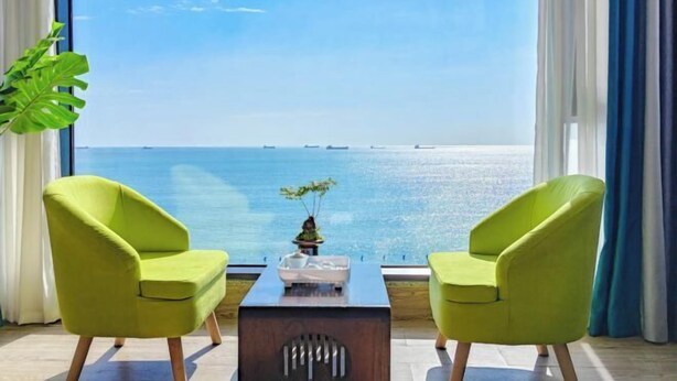 A room with two green armchairs facing a large window overlooking a body of water. - Dongshan Haizhiyuan Apartment (Dongshan County)