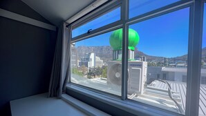 A room with a large window overlooking a cityscape, including a green spherical structure and a Samsung air conditioning unit. - M & B Backpackers (Cape Town)