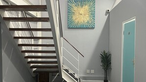 A modern staircase with wooden steps and a metal railing, a teal-colored wall with a sunburst painting, and a door with a number on it. - M & B Backpackers (Cape Town)