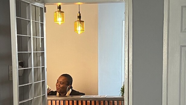 A reception area with a wooden counter, two hanging pendant lights, and a partially open door. - M & B Backpackers (Cape Town)