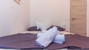 Een net opgemaakt bed met een paars dekbed en kussens, een houten deur en een klein nachtkastje met een lamp.