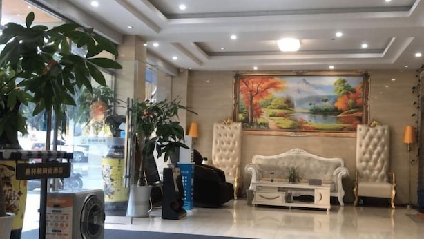 A hotel lobby with a sofa, armchairs, a painting, and potted plants.