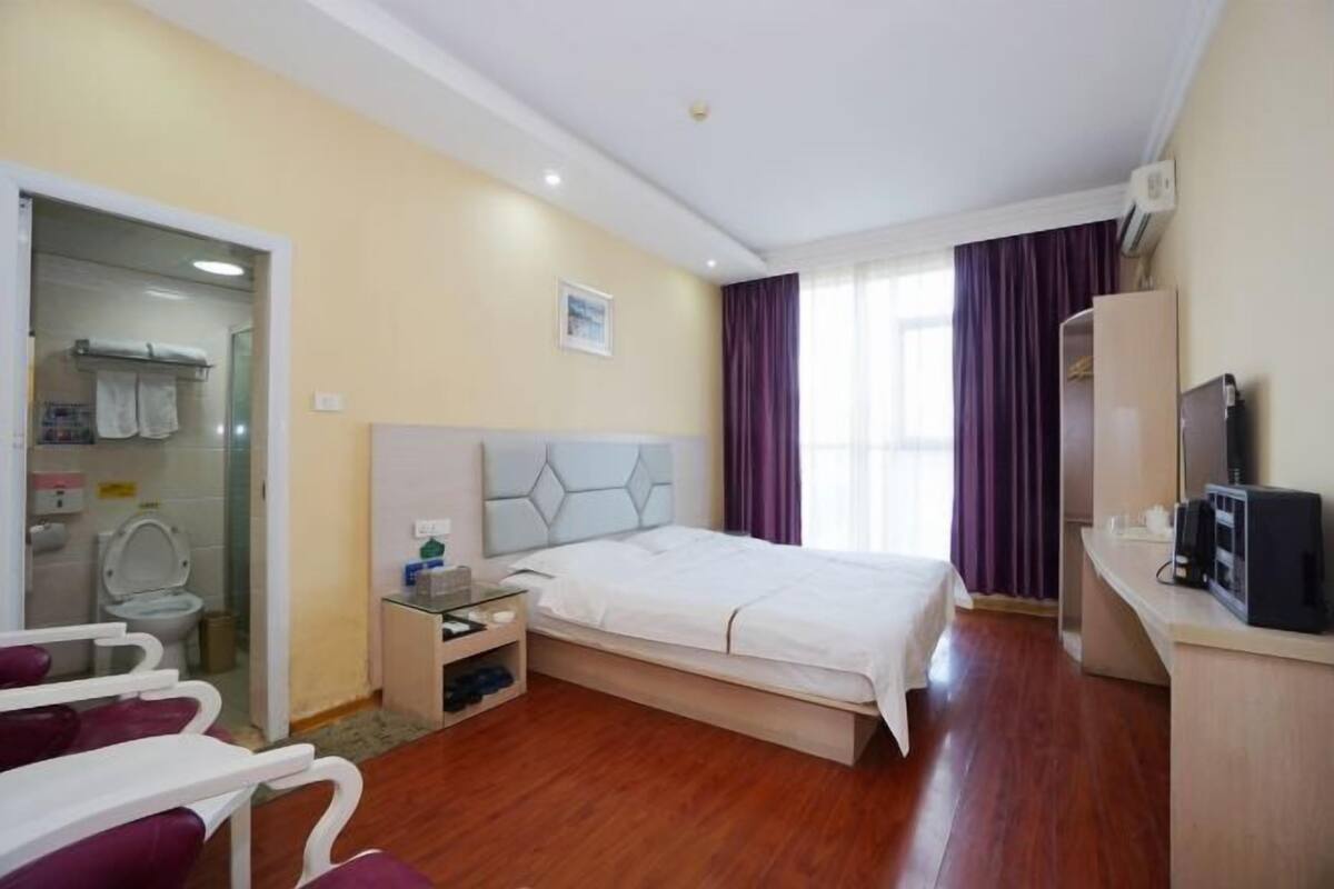 Ein Hotelzimmer mit Bett, Schreibtisch, Fernseher und einem Badezimmer mit Toilette sowie einer Duschkabine.