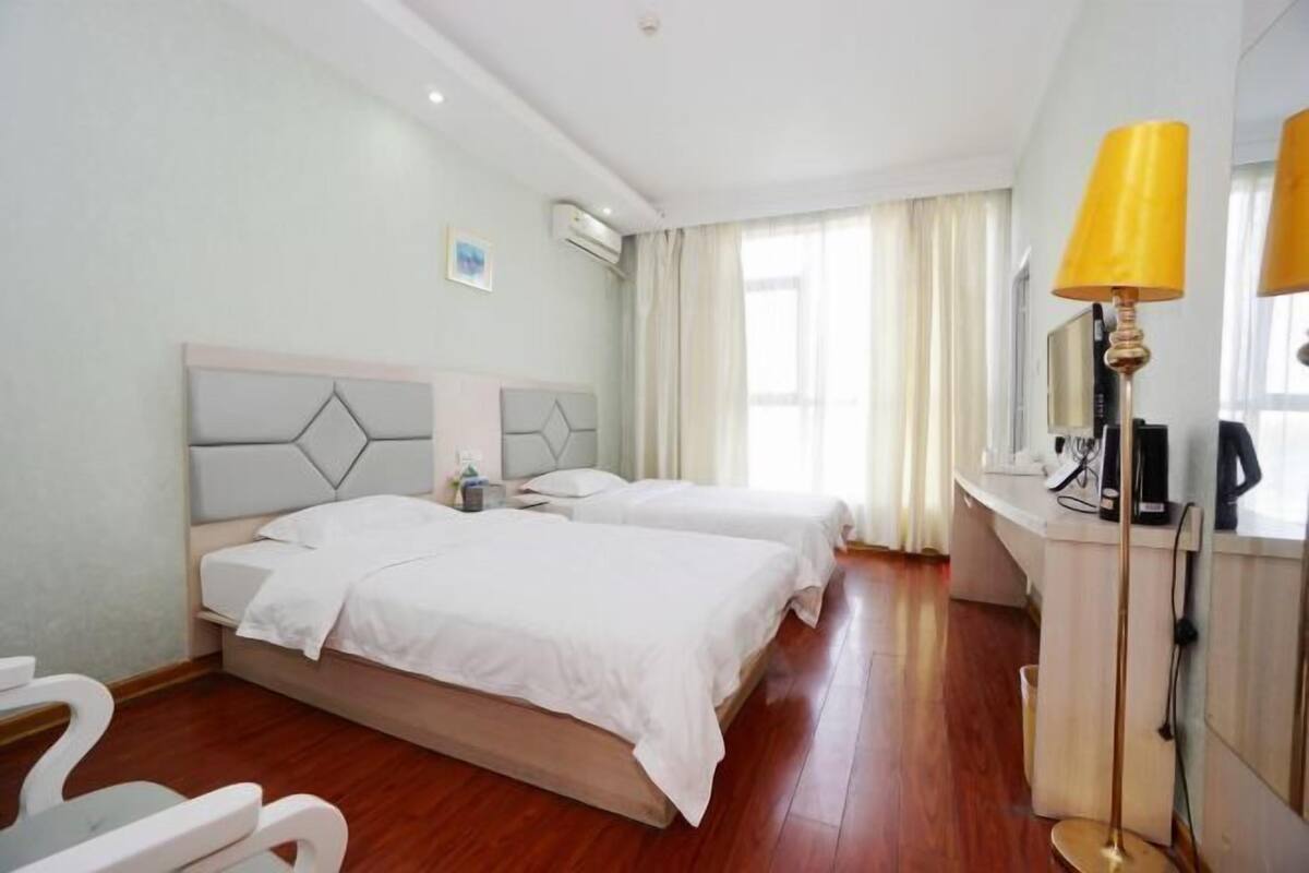 Ein Hotelzimmer mit zwei Betten, einem Schreibtisch, einem Stuhl, einer Lampe und einer Klimaanlage.