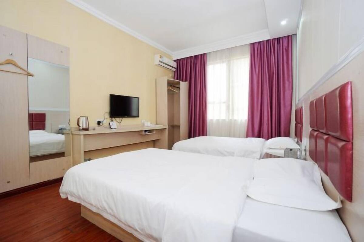Ein Hotelzimmer mit zwei Betten, einem Fernseher, einem Schreibtisch und einem Kleiderschrank.
