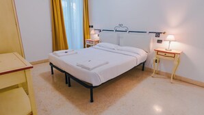 Un lit bien fait, avec du linge de lit blanc, deux tables de chevet avec des lampes et un rideau jaune.