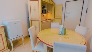 Une cuisine compacte équipée d’un four à micro-ondes, d’une cuisinière et de placards. On y trouve une table ronde avec des chaises et une bouteille d’eau posée dessus.