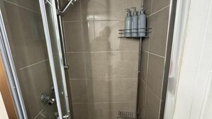 Ein kleiner, abgeschlossener Duschbereich mit Glastür, Handbrause und Ablage für Pflegeprodukte.