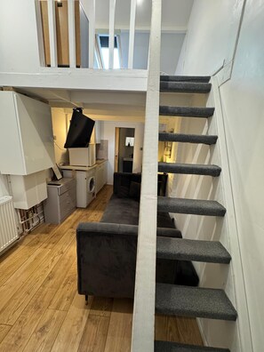 Un intérieur moderne avec un escalier, un canapé gris, un lave-linge et un coin cuisine.