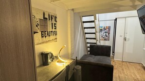 Ein kleines Zimmer mit Schreibtisch, Stuhl und Bett. An der Wand hängt ein Poster und ein Heizkörper ist angebracht.