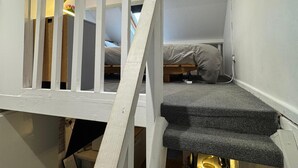 Ein gemütliches Schlafzimmer mit integriertem Bett, einem kleinen Schreibtisch und einer Treppe mit weißer Geländer.