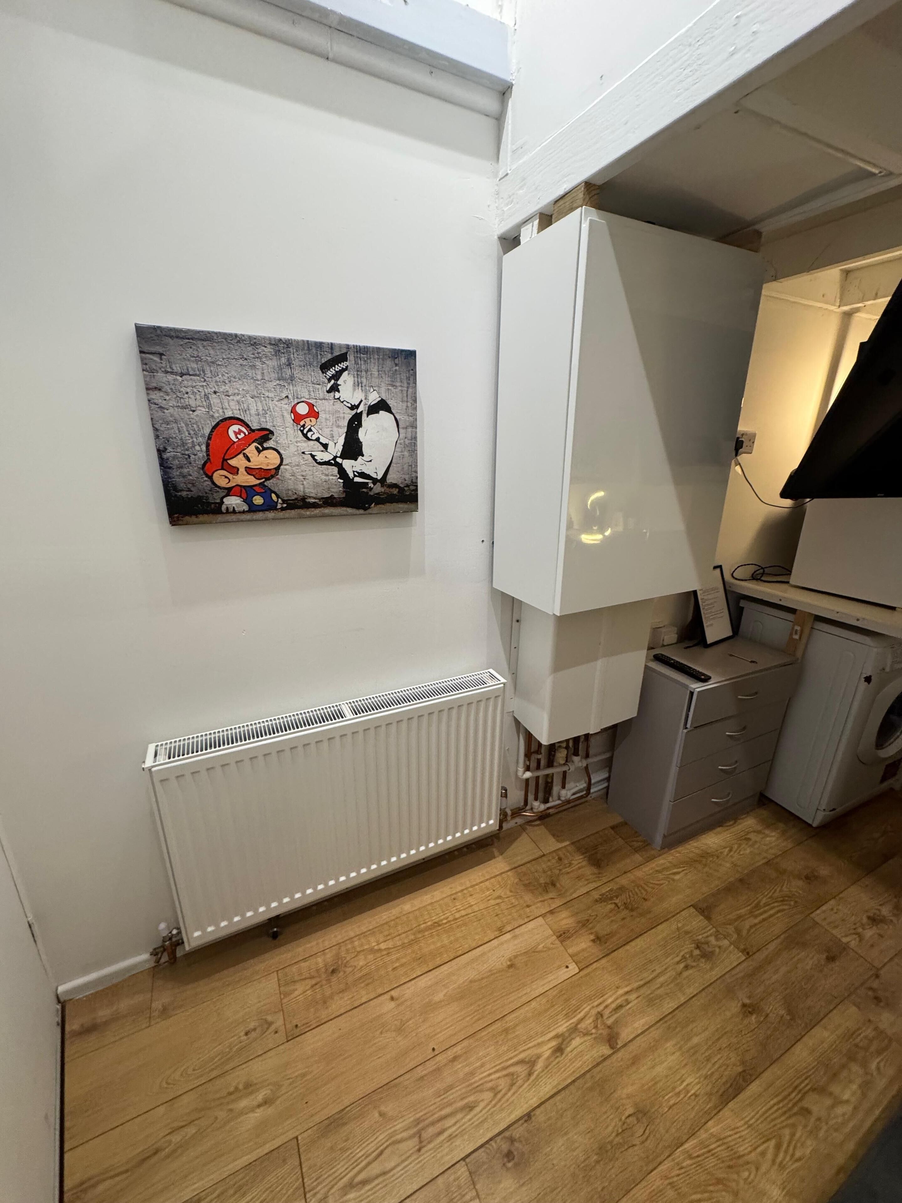 A compact kitchen with a radiator, a washing machine, and a painting of Mario and Bowser.