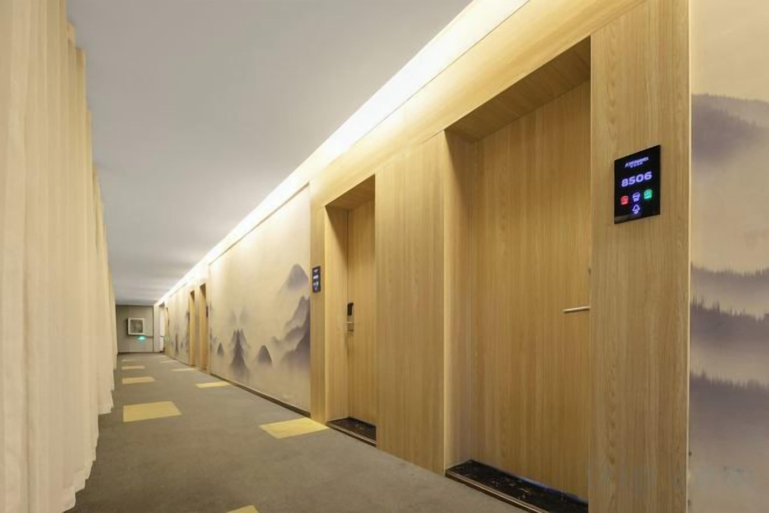 A hotel corridor with wooden doors, a digital elevator control panel, and a carpeted floor.