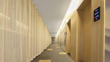 A hotel corridor with a long hallway, wooden walls, and a digital display on the right.