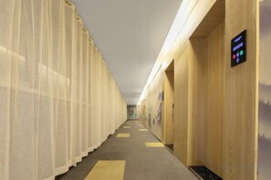 A hotel corridor with a long hallway, wooden walls, and a digital display on the right.