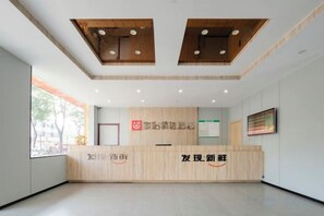 A reception area with a wooden reception desk, a framed artwork on the wall, and a window providing natural light.