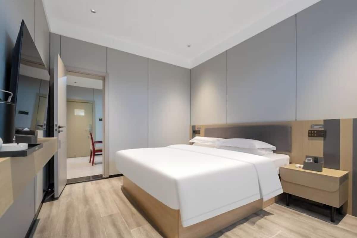 A modern hotel room with a large bed, a bedside table, a mirror, and a desk with a chair.